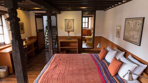Een slaapkamer met een groot bed, een houten bureau, een ladder en uitzicht op de badkamer.