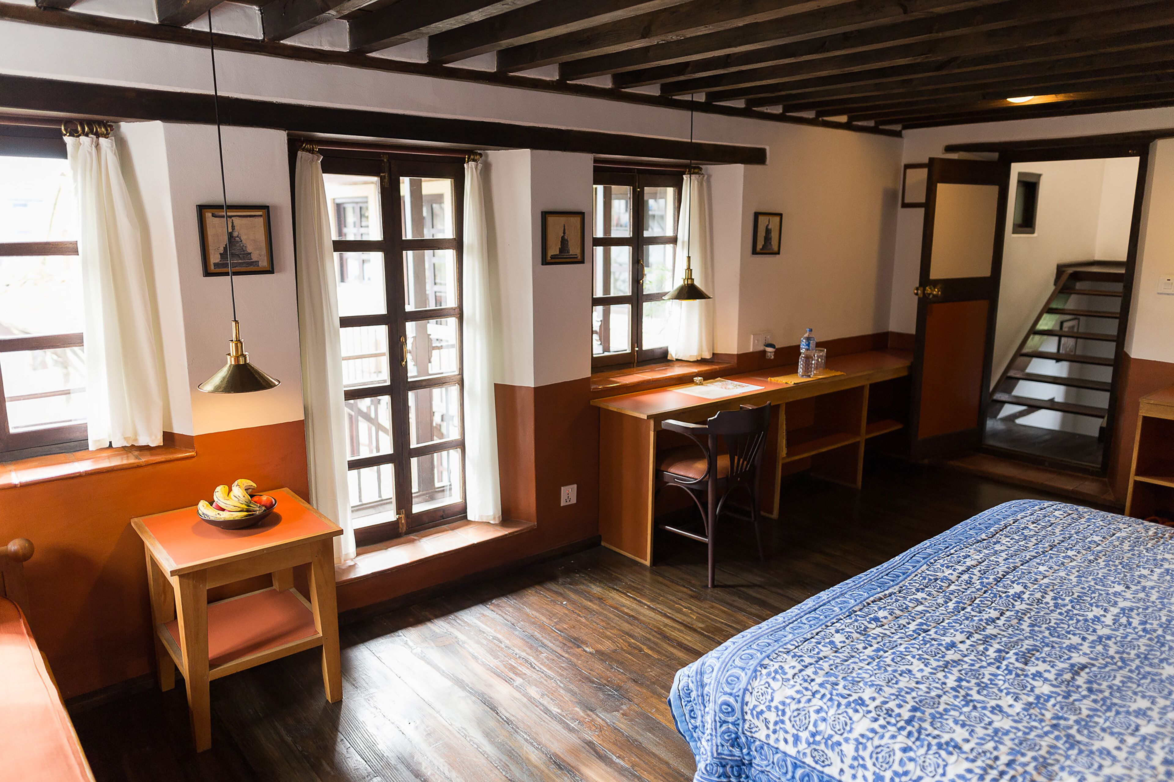 Una habitación con cama, escritorio, silla, ventana con cortinas y una escalera.