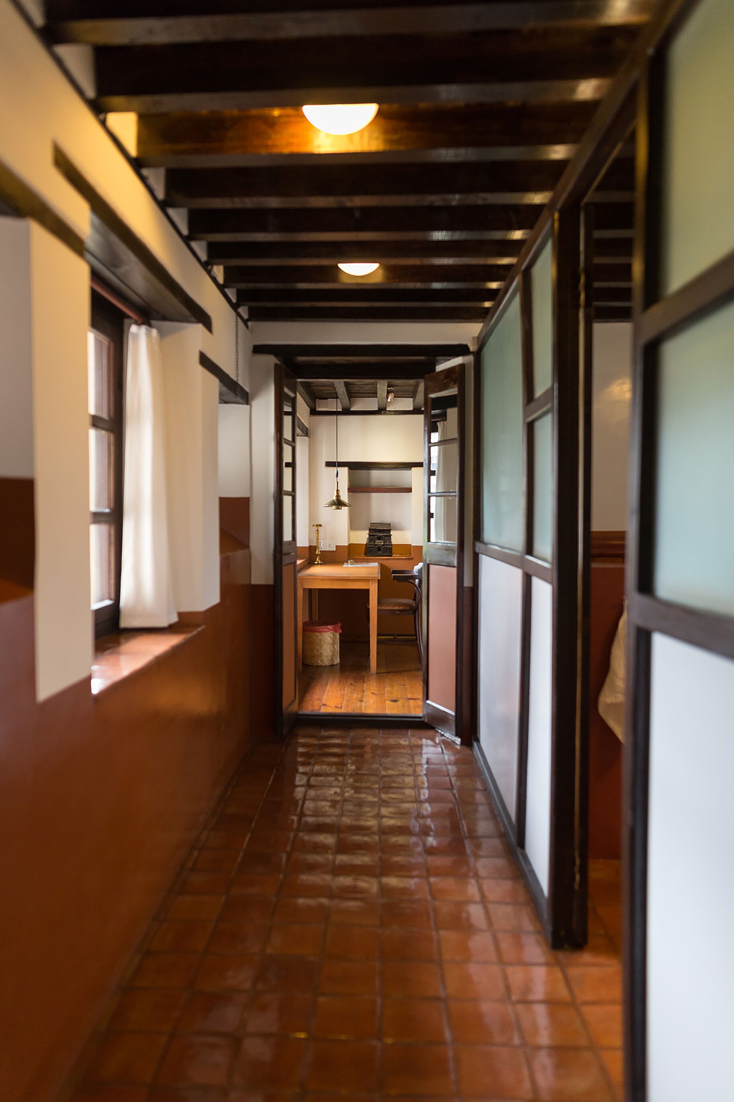 A narrow corridor with tiled flooring, wooden beams, and a window with a curtain.