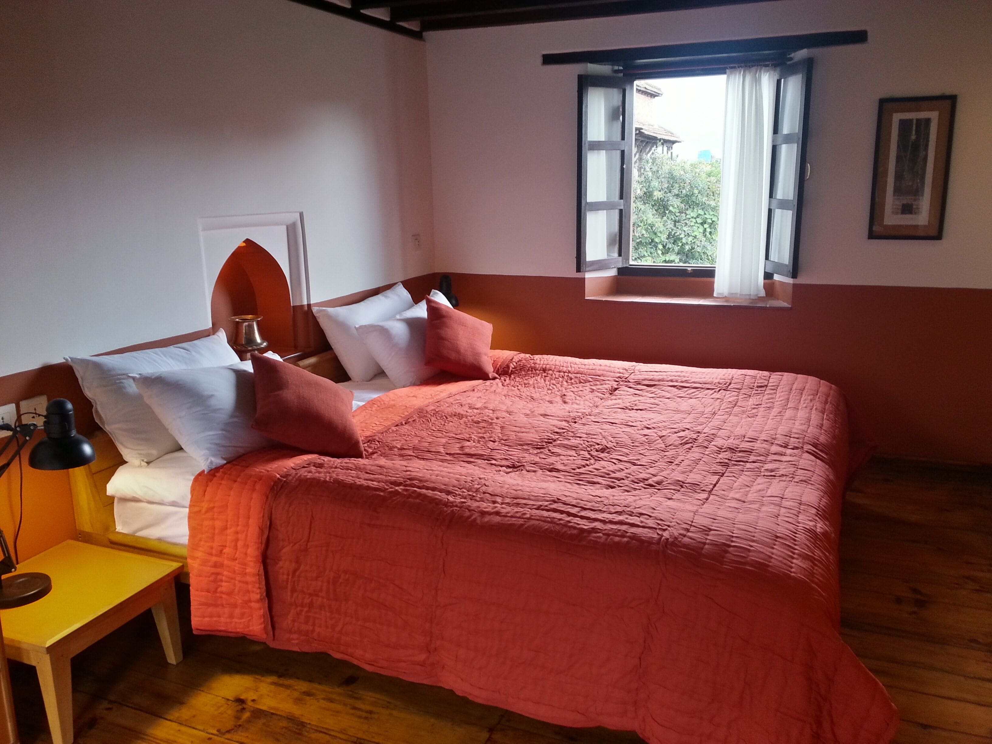 A bedroom with a bed, a nightstand, a lamp, a window with curtains, and a framed picture on the wall.