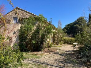 Ein aus Stein gebautes Haus mit Efeu, umgeben von einem Garten mit Kieswegen und Bäumen.