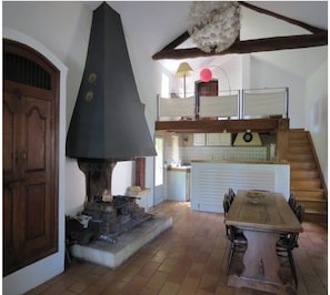 Eine rustikale Küche mit großem Kamin, einer Holztreppe und einem Essbereich mit Tisch und Stühlen.