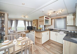 A caravan interior with a dining area, kitchen, and living space, featuring wooden furniture and a flat-screen TV. - 2 bedroom accommodation in Axminster (Axminster)