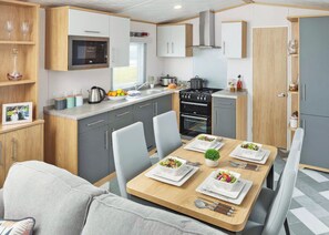 Une cuisine compacte équipée d’un four à micro-ondes, d’une cuisinière et d’un évier, une table à manger avec des assiettes et des couverts, et un canapé au premier plan.