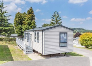 Une maison mobile de plain-pied, dotée d’un porche à l’avant, d’une cheminée et du numéro « 79 » peint sur le côté.