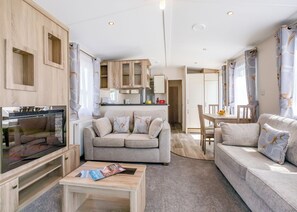 A compact living space with a sofa, a coffee table, a TV, and a kitchen area. - 2 bedroom accommodation in Axminster (Axminster)