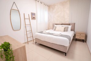 A neatly arranged bedroom with a bed, bedside tables, a mirror, a ladder, and a potted plant.