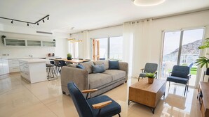 Un salon moderne comprenant un canapé, des fauteuils, une table basse et un coin cuisine avec des placards et une table à manger.