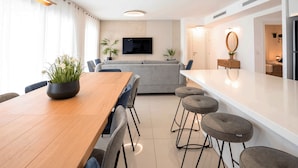 Un salon moderne avec une table à manger en bois, un canapé gris et des tabourets de bar.