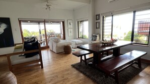 A spacious living room with a wooden floor, a dining table with benches, a sofa, and a large window providing a view of the outdoors. - Brenton Bliss, beach view, walk to beach, safe secluded area on the Garden Route (Knysna)