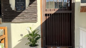 A building entrance with a wooden wall, a blackboard with a welcome message, a metal gate, a potted plant, a green pet bowl, and a tiled step. - Brenton Bliss, beach view, walk to beach, safe secluded area on the Garden Route (Knysna)