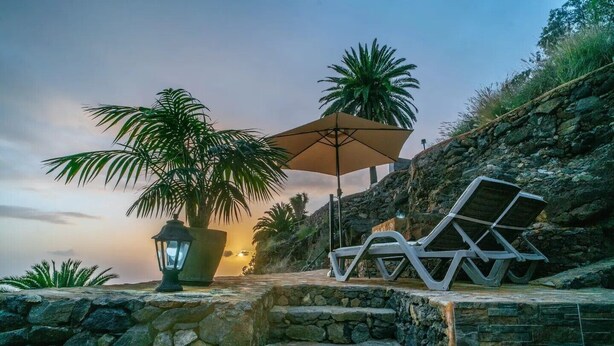 Un chemin de pierres, des fauteuils de jardin, un grand parasol et une plante en pot.