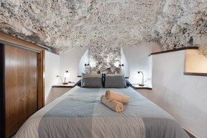 A bedroom with a textured ceiling, a bed with a blue and white bedspread, two rolled towels, and bedside lamps.