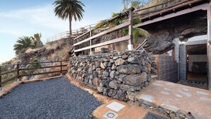 Un mur de soutènement en pierre agrémenté d’une rambarde métallique, un chemin de gravier et une entrée d’immeuble avec une façade en pierre.