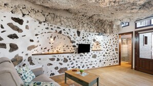 Une pièce avec un mur en pierre, un téléviseur à écran plat, une table en bois et un canapé.