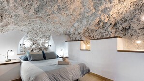 Une chambre à coucher dotée d’un plafond en pierre unique, d’un lit avec une couette grise et blanche, de tables de chevet avec des lampes et d’un plancher en bois.