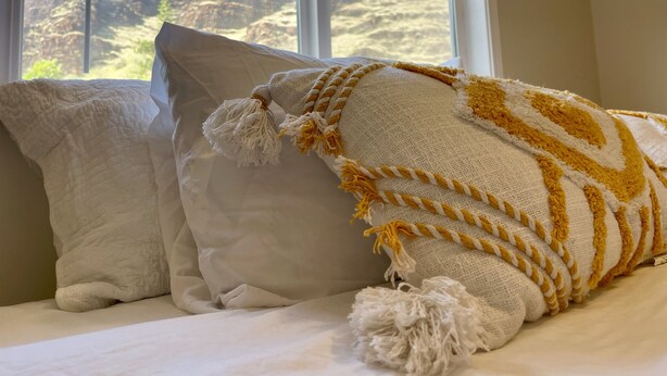 Un lit avec des oreillers blancs et une couverture à motifs jaunes et blancs.