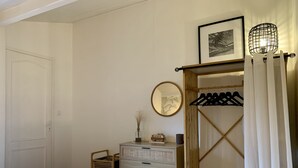 Un dormitorio con cama, cómoda, espejo, lámpara colgante y perchero.