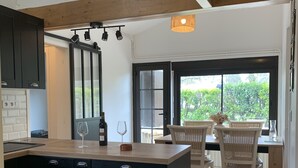 Una cocina moderna con una isla central, armarios negros y un comedor con sillas de mimbre y vistas a zonas verdes.