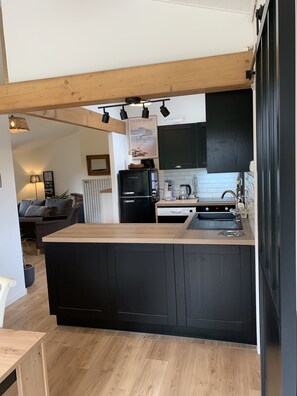 A modern kitchen with black cabinetry, a wooden island, and a dining area with a table and chairs. - Comfortable house between Dune du Pyla, ocean and lake (La Teste-de-Buch)