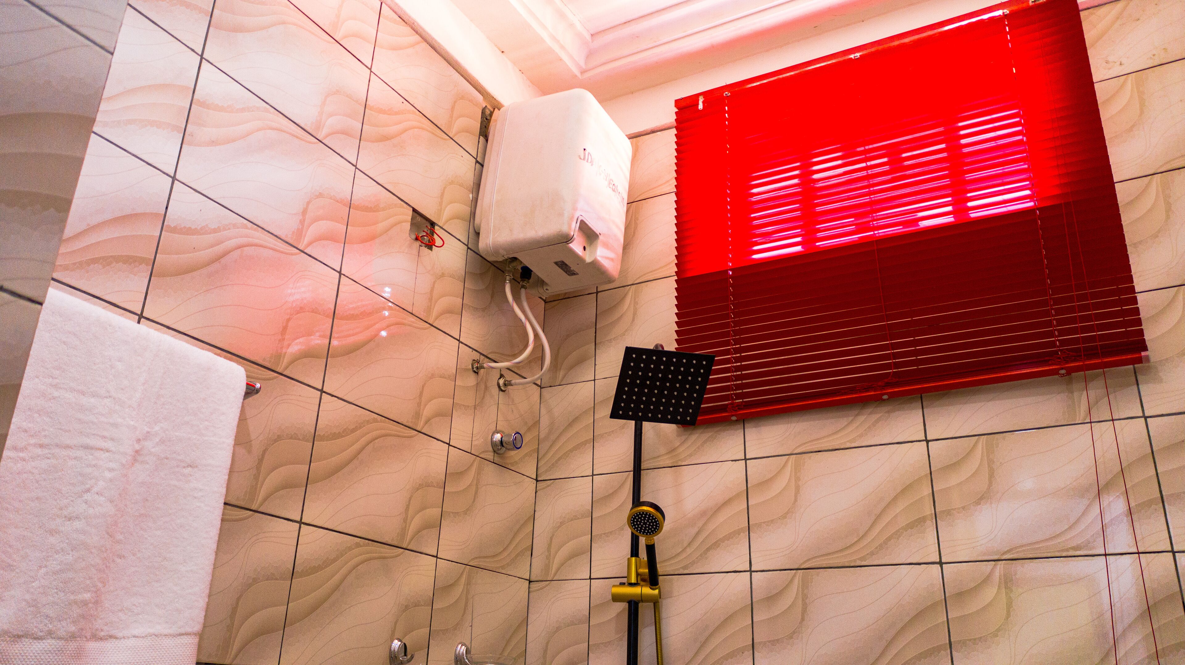 A bathroom with a marble floor, a handheld showerhead, a towel rack, and a red light fixture.