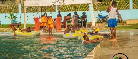 Un área de piscina con gente en flotadores y una zona de estar cubierta.