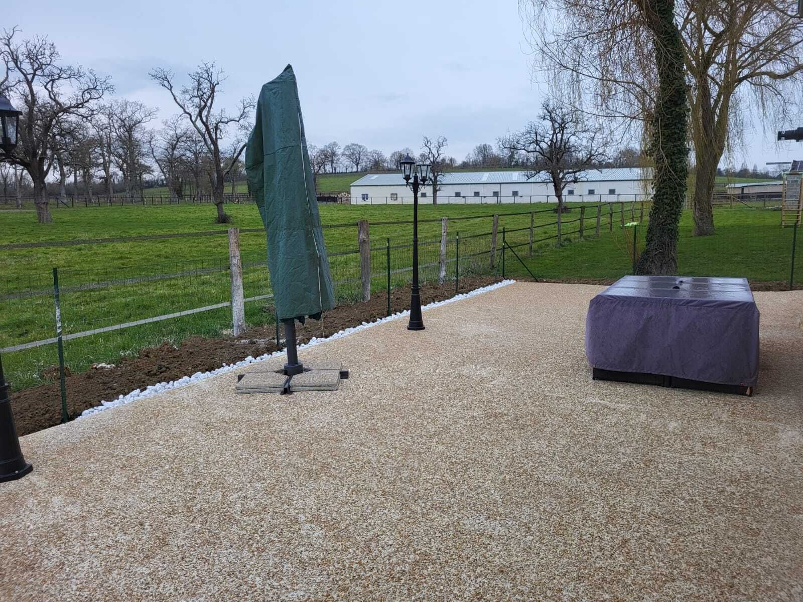 Een terras met een overdekte tafel en stoel, omringd door een grindpad en een hek.