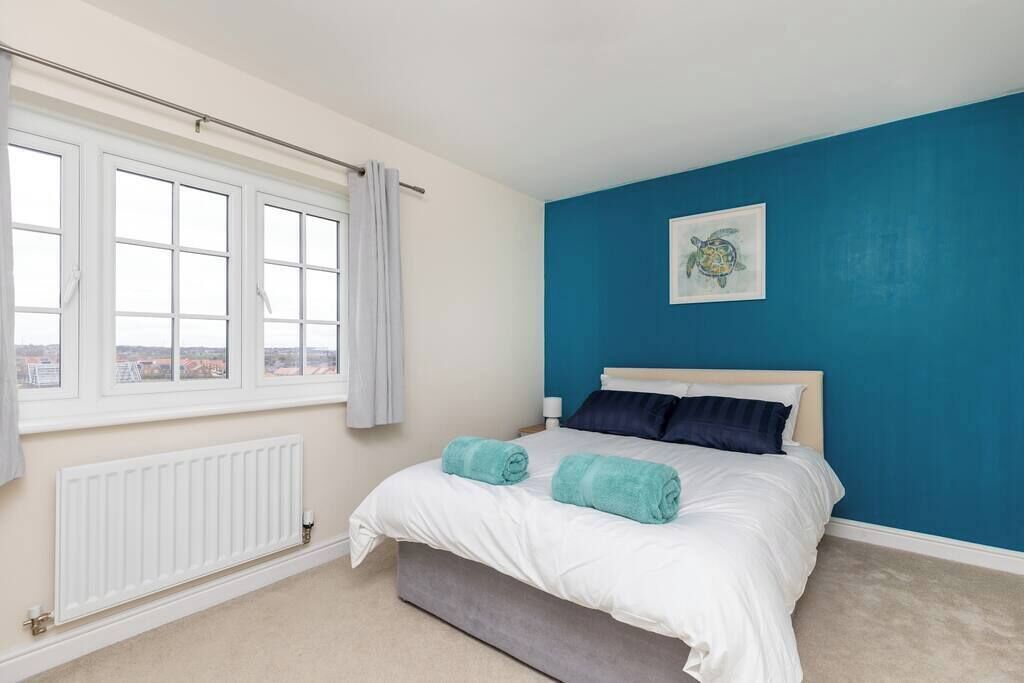 A bedroom with a bed, a window with curtains, a radiator, and a blue wall with a turtle painting.
