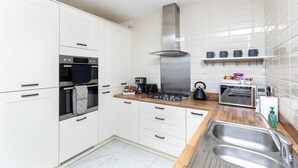 Une cuisine moderne avec des armoires blanches, une hotte de cuisinière en acier inoxydable, un four encastré, une machine à café et un grille-pain.