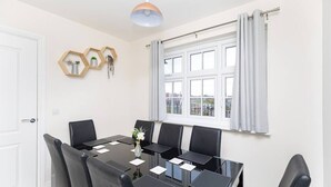 Une salle à manger avec une table rectangulaire, six chaises et une fenêtre avec des rideaux.