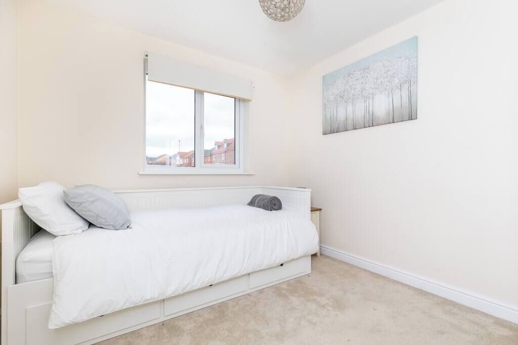 A bedroom with a white bed, a window, and a painting on the wall.