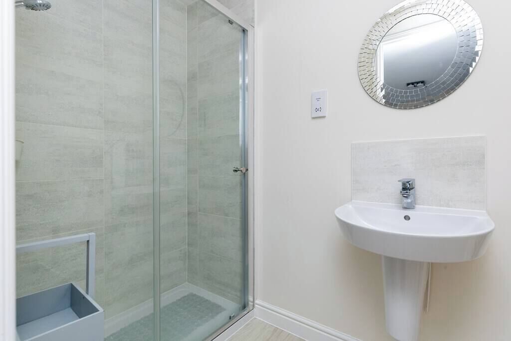 A bathroom with a glass shower enclosure, a white sink, and a mirror with a mosaic frame.