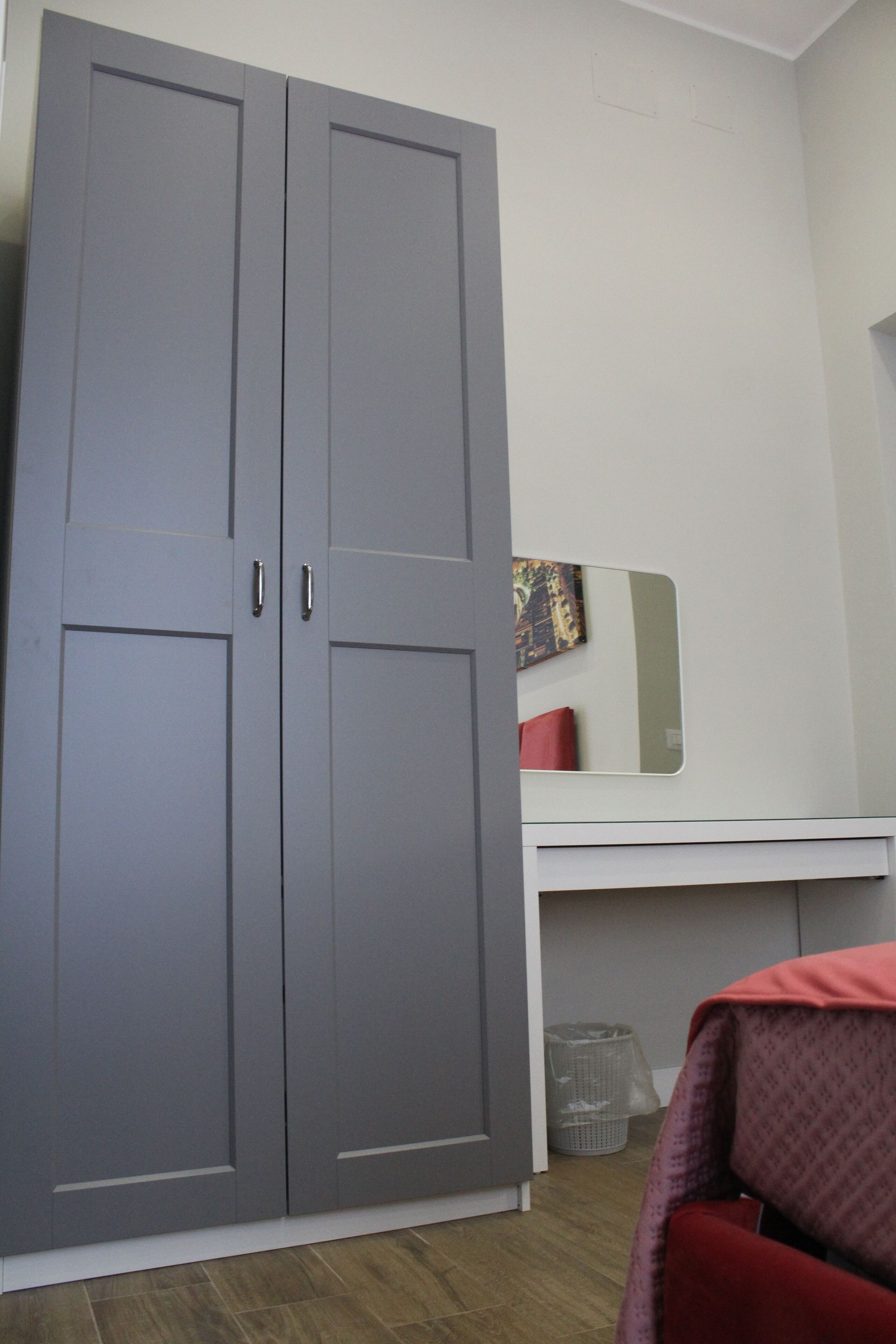 Et værelse med en grå garderobe, et hvidt skrivebord og et spejl.