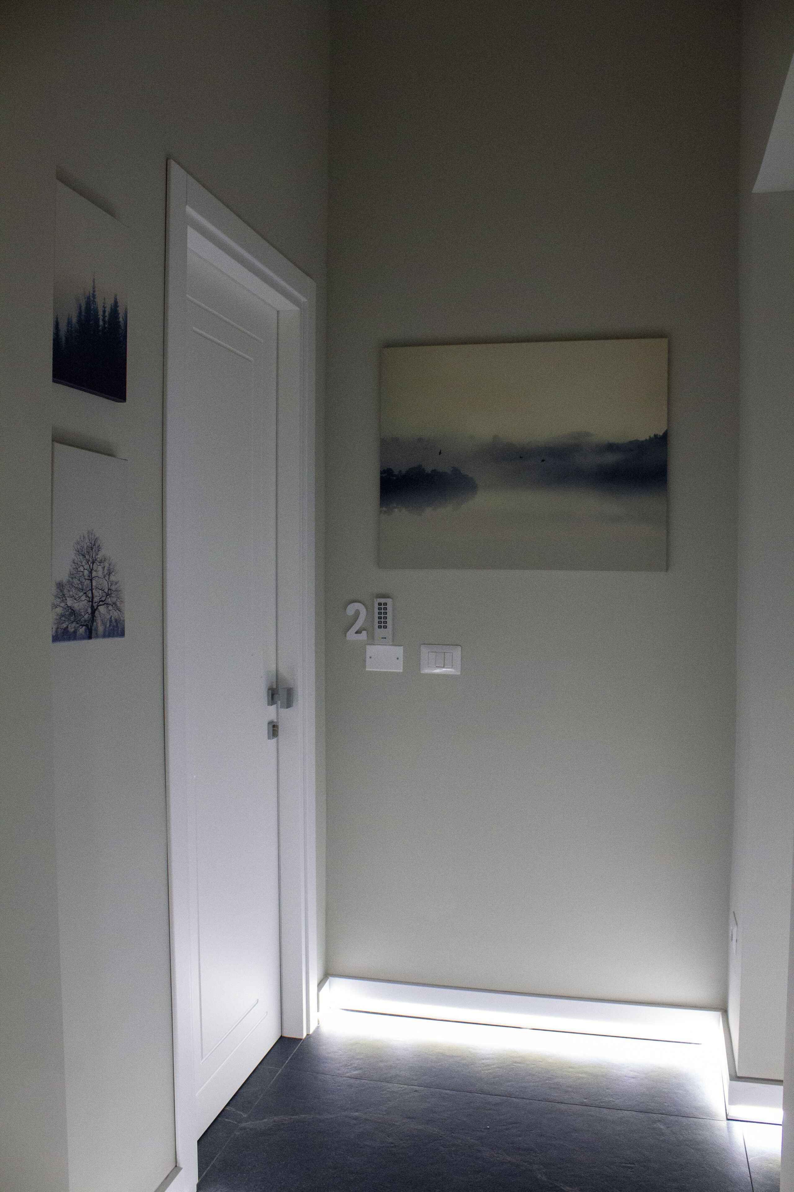 Un pasillo con una puerta blanca, un cuadro de un paisaje y un cartel con el número 2.