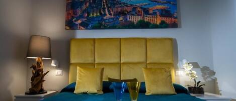 A hotel room with a bed, a painting of a cityscape, a lamp, and a bottle of champagne.