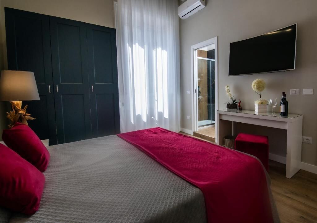Une chambre à coucher avec un lit, un bureau, une télévision et une fenêtre avec des rideaux.