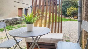 Un petit espace extérieur aménagé avec une table ronde et deux chaises, un pot de fleurs et une clôture en bois en arrière-plan.