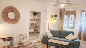 Un salon avec un canapé vert, un fauteuil en osier, une table basse en bois et une étagère blanche agrémentée d’objets décoratifs.