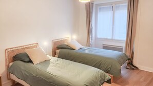 Une chambre avec deux lits simples, une fenêtre avec des rideaux et un luminaire suspendu.