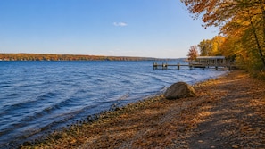 A lakeside view with a dock, a large rock, and autumn foliage.
