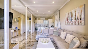 A spacious living room with a large sofa, a coffee table, and a TV. There is a kitchen in the background with cabinets and a dining area. - Katerina's Place (ARGOS)