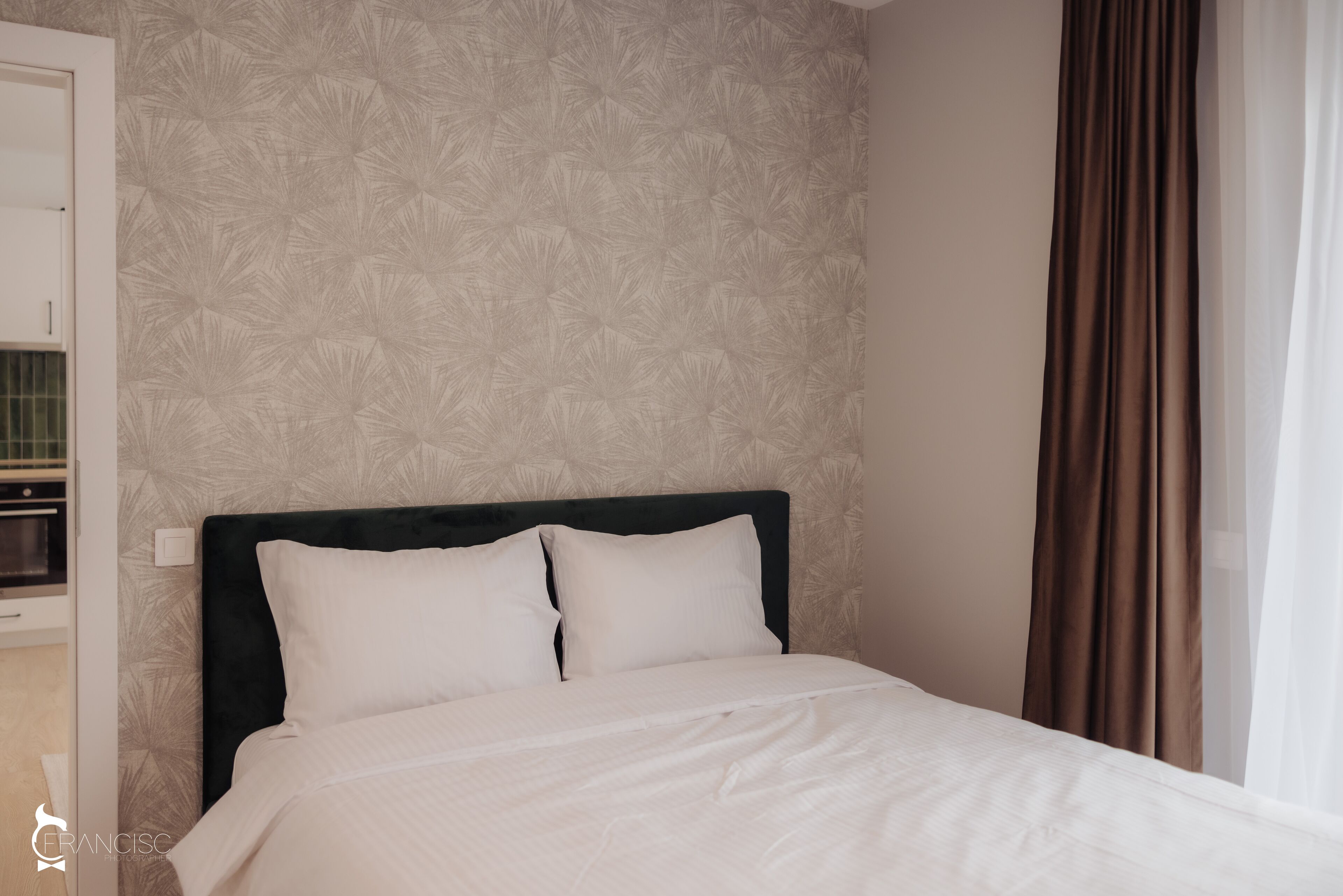 A neatly made bed with white linens in a room with a patterned wallpaper and a dark headboard.