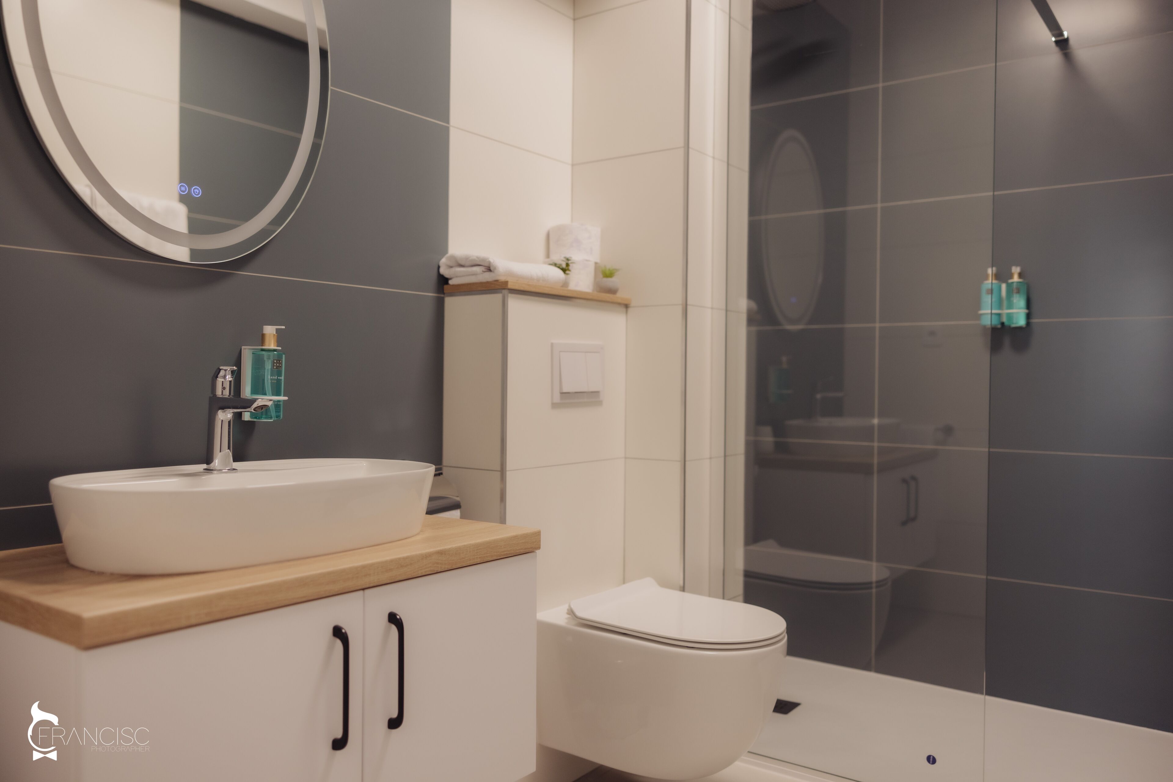 Een moderne badkamer met een ronde spiegel, een wastafel, toilet en een douchehoek.