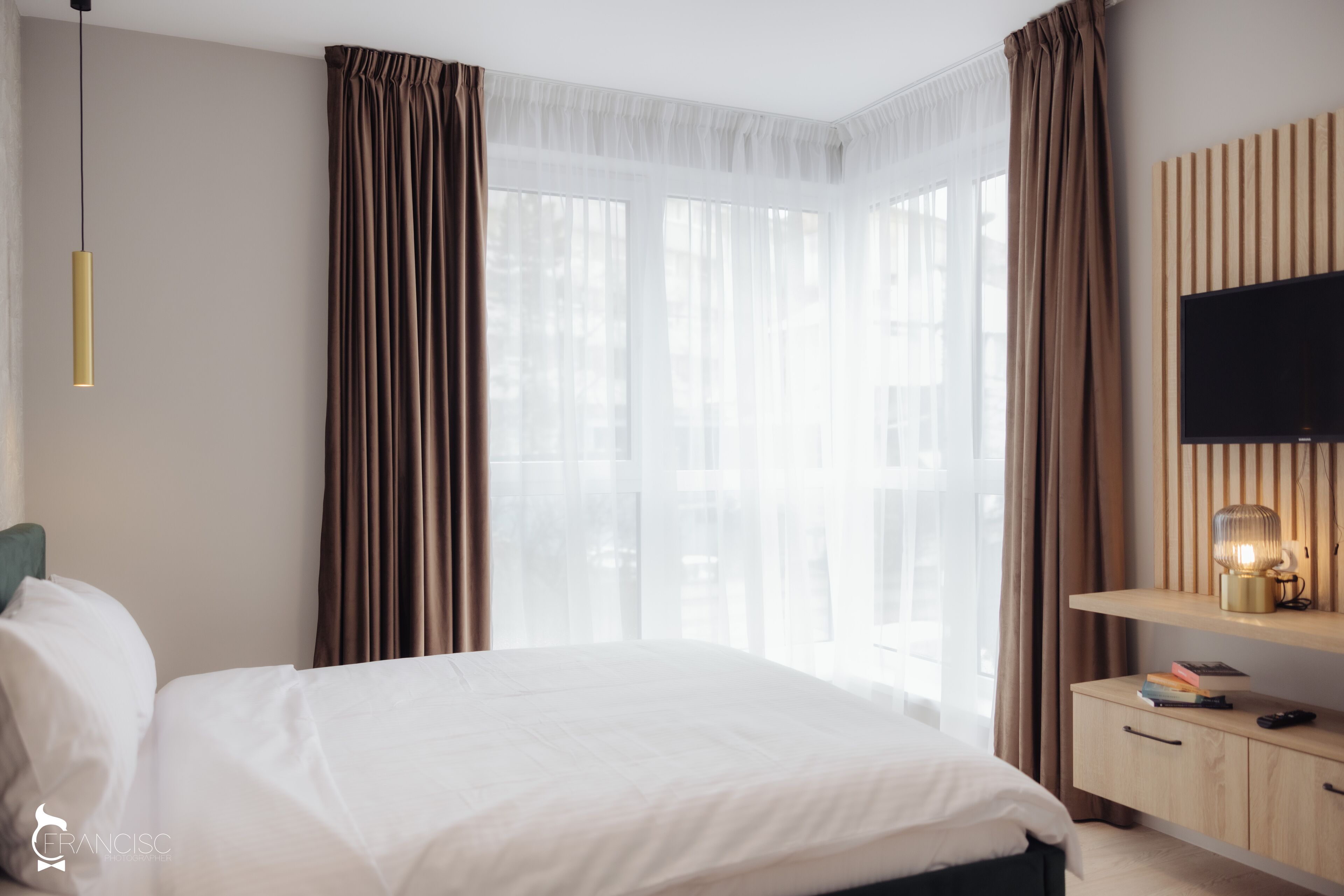 A hotel room with a bed, a TV on a wooden shelf, and a window with curtains.