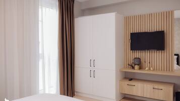 A bedroom with a bed, a wardrobe, a TV mounted on a wooden panel, and a bedside table with a lamp.