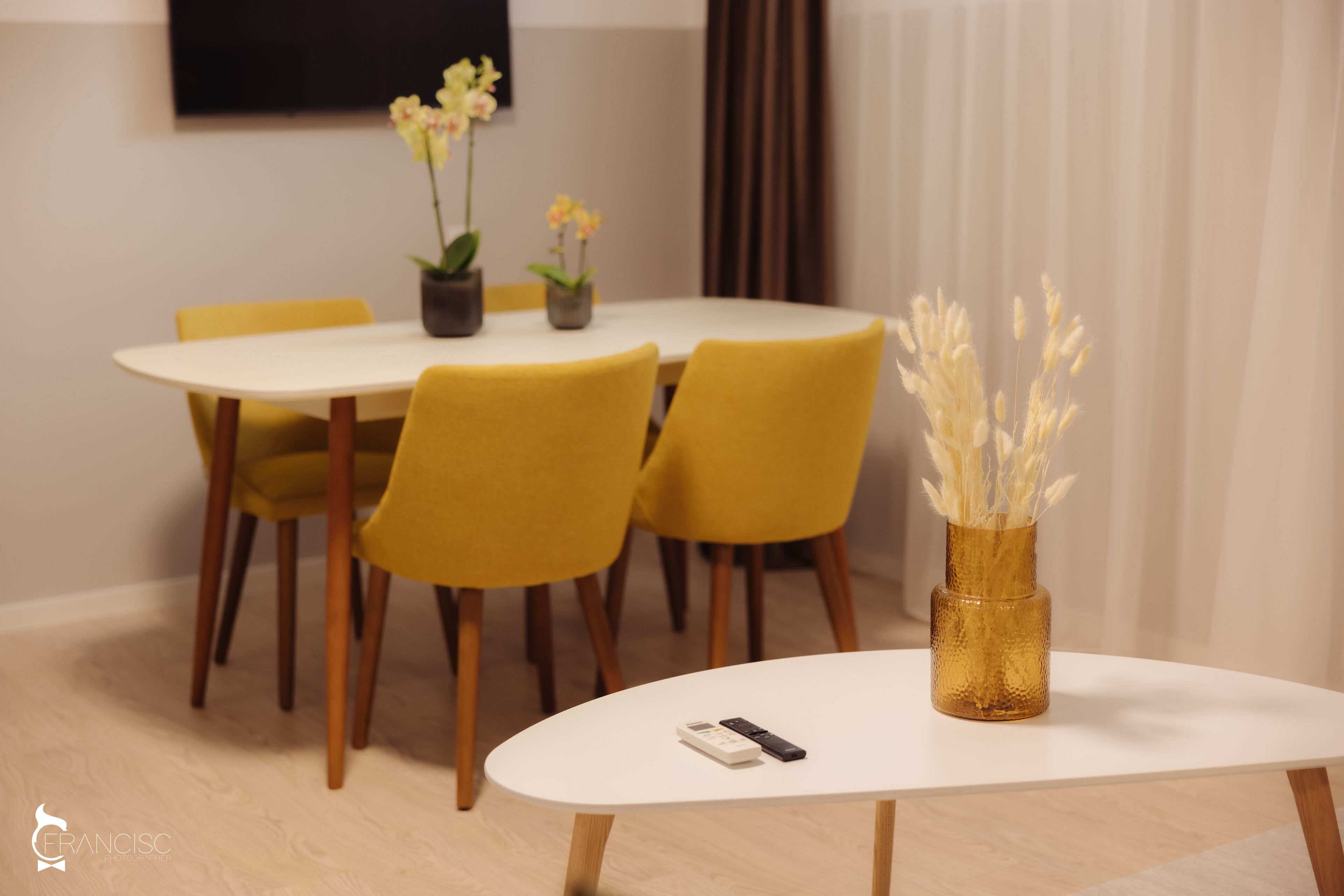 A dining area with a round table, yellow chairs, and a vase with dried plants.