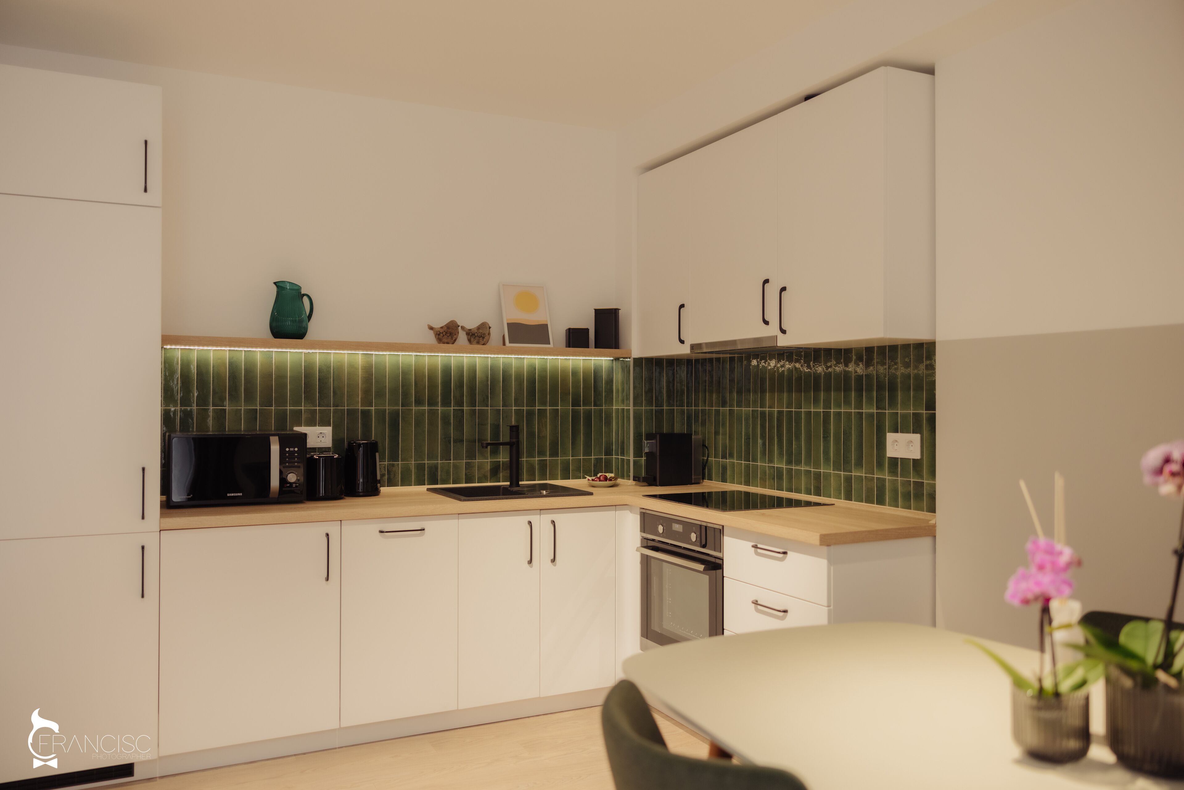 Una cocina moderna con armarios blancos, salpicadero verde y encimera de madera.