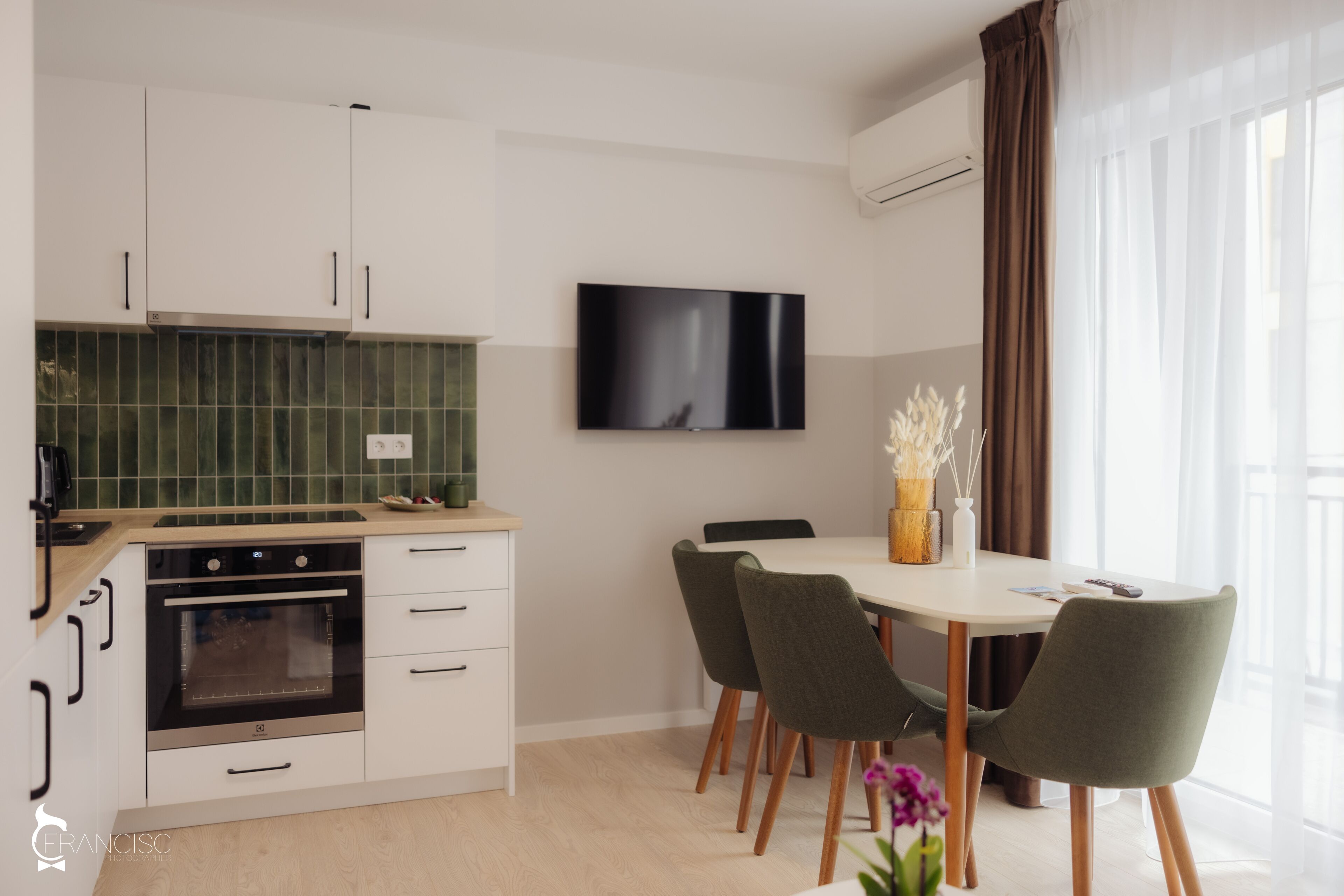 A modern kitchen with white cabinets, a built-in oven, and a flat-screen TV mounted above the counter.