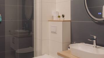 A modern bathroom with a glass shower enclosure, a white toilet, a sink with a wooden countertop, and a mirror with a circular frame.