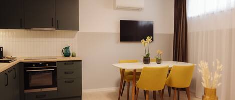A modern kitchen with dark cabinets, a built-in oven, and a dining area with yellow chairs and a small table.